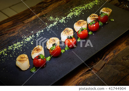 Fried scallops with tomatoes on a black plate. Shallow dof. Fried scallops with tomatoes on a black plate. Shallow dof. 41744904