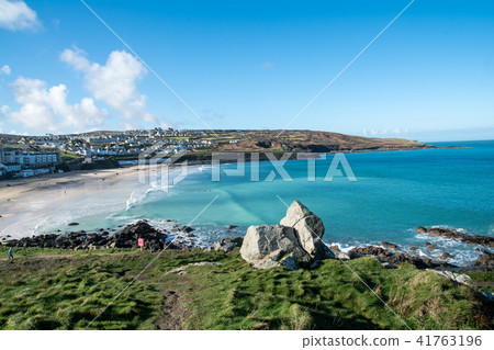 一個被岩石和山丘環繞的淺沙灘淡藍色的海岸和山頂上的城市景觀，可以在遠處看到在英國的郊區 41763196
