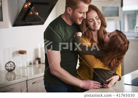 Happy parents hugging daughter in kitchen Happy parents hugging daughter in kitchen 41765030