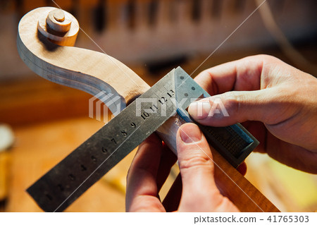 Master artisan luthier working on creation of a violin scroll. detailed work on wood with tools. 41765303
