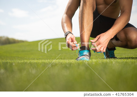 Sportsman is tying shoe laces on grass Sportsman is tying shoe laces on grass 41765304