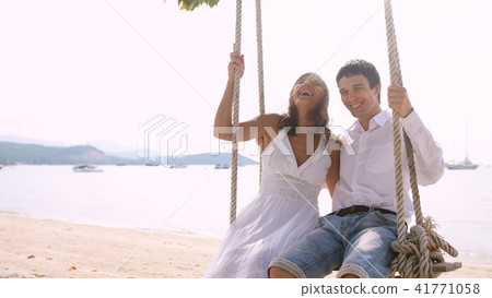Young joyful couple rest on a swing at the tropical beach against the sea on holiday vacation 41771058