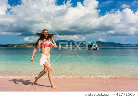 Happy young woman walking through shallow sea water on the beach 41771500