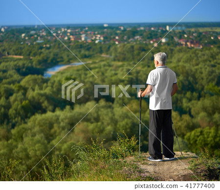 Old man watching the city panorame keeping tracking sticks. Old man watching the city panorame keeping tracking sticks. 41777400