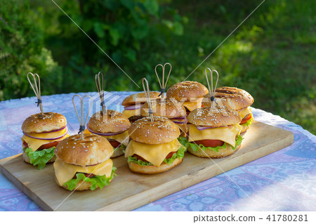 Tasty burgers with cheese, lettuce, onion and tomatoes served outdoor on a wooden table. Tasty burgers with cheese, lettuce, onion and tomatoes served outdoor on a wooden table. 41780281