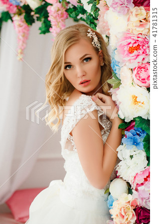 Young woman wearing wedding dress posing in room decorated with flowers Young woman wearing wedding dress posing in room decorated with flowers 41781315