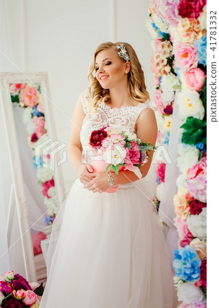 Young woman wearing wedding dress posing in room decorated with flowers Young woman wearing wedding dress posing in room decorated with flowers 41781332