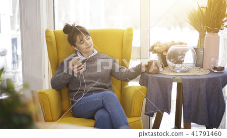 A young girl sitting in a big chair with a phone listening to music A young girl sitting in a big chair with a phone listening to music 41791460