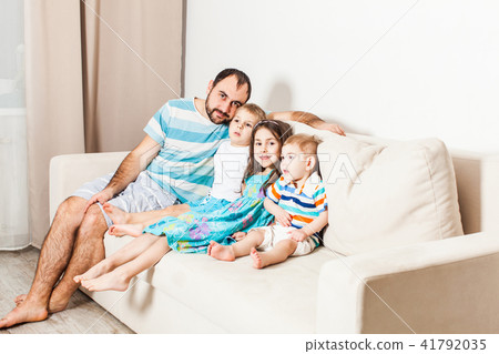 Young man sitting with three children on the couch in the living room. 41792035