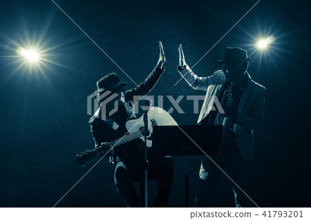 Musician Duo band doing Hand coordination when playing a Trumpet and singing a song and playing the guitar on black background with spot light and lens flare, musical concept Musician Duo band doing Hand coordination when playing a Trumpet and singing a song and playing the guitar on black background with spot light and lens flare, musical concept 41793201