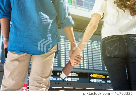 Closeup hands of asian couple holding the passport over the photo bluured of flight information on the bug board in modern an airport, travel and transportation with technology concept. 41793325