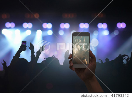 Female hand holding mobile smart phone taking video record or Live stream of Concert crowd with super star songer and silhouettes of Music fanclub with show hand action, musical and concert concept Female hand holding mobile smart phone taking video record or Live stream of Concert crowd with super star songer and silhouettes of Music fanclub with show hand action, musical and concert concept 41793342