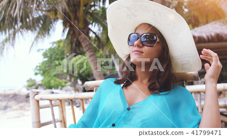 Young elegant woman wearing hat and sunglasses on holiday, sitting in beach cafe Young elegant woman wearing hat and sunglasses on holiday, sitting in beach cafe 41799471