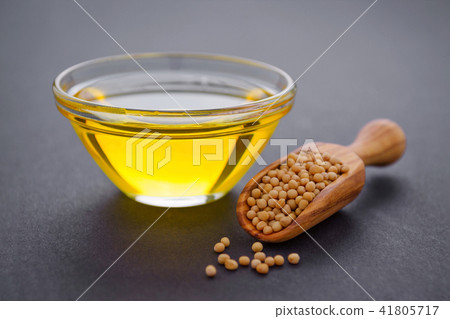 mustard seeds in a wooden scoop and glass bowl with oil on dark background 41805717