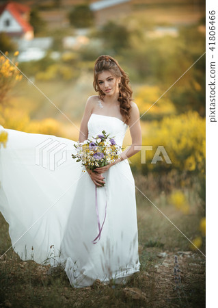 Beautiful young bride is wearing white dress holding fashion bouquet of wildflowers in yellow field Beautiful young bride is wearing white dress holding fashion bouquet of wildflowers in yellow field 41806466