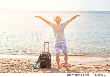 Man tourist in summer clothes with a suitcase in his hand, looking at the sea on the beach, concept 41809778