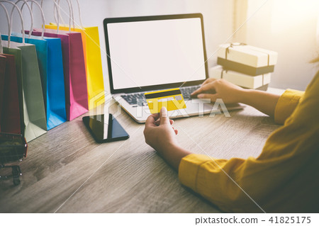 Young woman typing laptop for online shopping website and holdin Young woman typing laptop for online shopping website and holdin 41825175