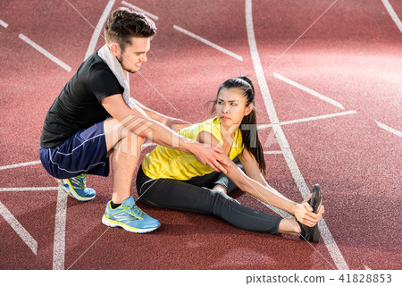 Man and woman on cinder track of sports arena stretching exercises Man and woman on cinder track of sports arena stretching exercises 41828853