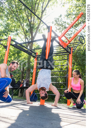 Determined young man practicing handstand motivated by his friends Determined young man practicing handstand motivated by his friends 41828876