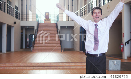 Happy handsome businessman stands with raising hands from joy in modern office. Concept of business Happy handsome businessman stands with raising hands from joy in modern office. Concept of business 41829733