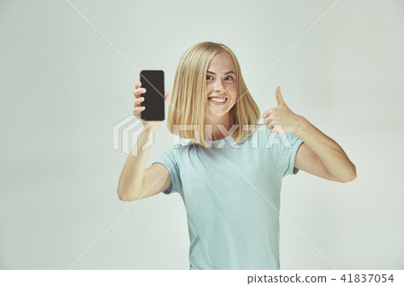 Portrait of a confident casual girl showing blank screen mobile phone isolated over gray background Portrait of a confident casual girl showing blank screen mobile phone isolated over gray background 41837054