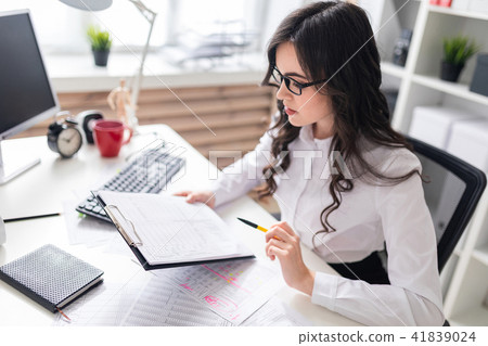 A young girl sits at the office desk and checks documents. 41839024