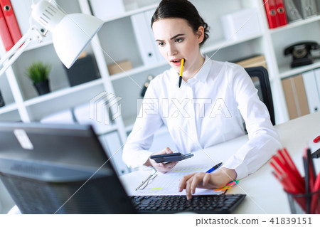 A young girl in the office holds a pen in her mouth and works with a calculator, documents and a 41839151