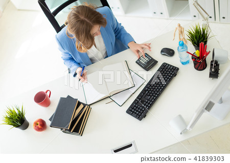 Beautiful young girl sitting at desk in office, holding a pen in her hand and reading a book. Beautiful young girl sitting at desk in office, holding a pen in her hand and reading a book. 41839303