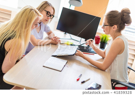 A young girl sits at a table in her office and talks to two co-partners. The girl is holding a A young girl sits at a table in her office and talks to two co-partners. The girl is holding a 41839328