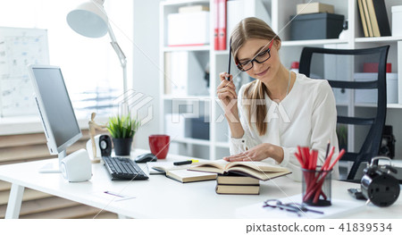 A young girl sits at a table in the office and holds a pencil in her hand. Before the girl lies an A young girl sits at a table in the office and holds a pencil in her hand. Before the girl lies an 41839534