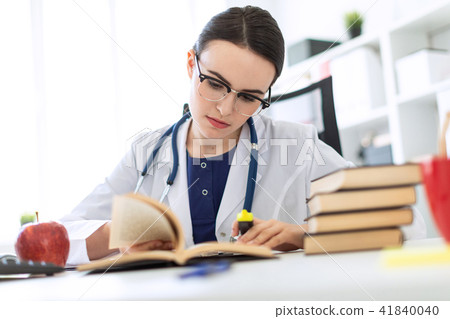 A beautiful young girl in a white robe is sitting at the computer desk with a marker and a book. A 41840040