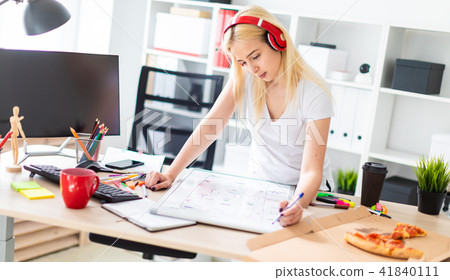 A young girl in the headphones stands near the table and holds a marker in her hand. On the table is A young girl in the headphones stands near the table and holds a marker in her hand. On the table is 41840111