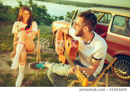 Couple sitting and resting on the beach playing guitar on a summer day near river Couple sitting and resting on the beach playing guitar on a summer day near river 41841669