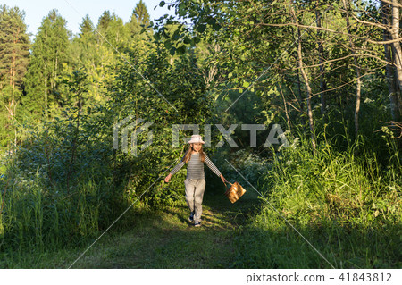 Young girl walking on a path through green woods carrying a basket 41843812