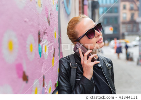 Woman talking on smartphone leaning against colorful graffiti wall in New York city, USA. Woman talking on smartphone leaning against colorful graffiti wall in New York city, USA. 41844111