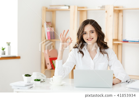 Young business woman showing ok sign sitting in the modern office with labtop. Young business woman showing ok sign sitting in the modern office with labtop. 41853934