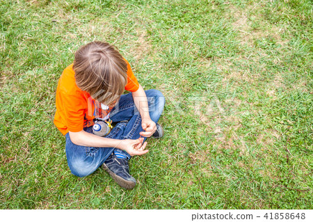 Single bored teen boy sitting on grass Single bored teen boy sitting on grass 41858648