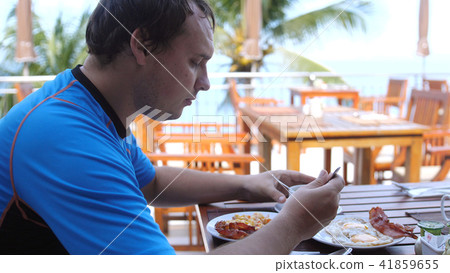 Young man eating american breakfast sitting in a beach cafe 41859655