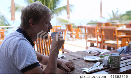 Young handsome sad man eating breakfast sitting in a beach cafe drink tea 41868826