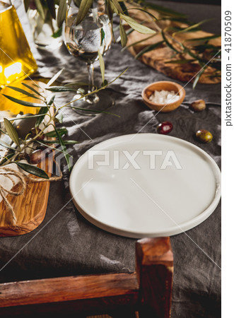 Table setting with gray Linen tablecloth and napkin, white plate, cutlery and and olive tree branch Table setting with gray Linen tablecloth and napkin, white plate, cutlery and and olive tree branch 41870509