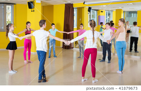 Teenage boys and girls practicing circle dance with female trainer in dance hall 41879673