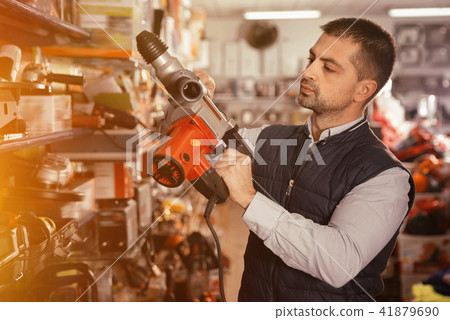 Adult male is standing with puncher in tools store. Adult male is standing with puncher in tools store. 41879690