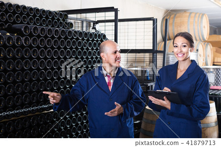 portrait of expert woman standing with clipboard and talking to winemaker in cellar portrait of expert woman standing with clipboard and talking to winemaker in cellar 41879713