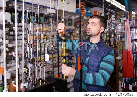 thoughtful male choosing fishing rod for fishing in the sports shop 41879835
