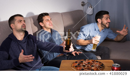 Happy men emotionally watching tv with beer and pizza at home Happy men emotionally watching tv with beer and pizza at home 41880029