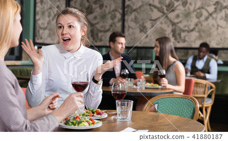 Happy attractive girl emotionally discussing with female friend while dining in cozy restaurant Happy attractive girl emotionally discussing with female friend while dining in cozy restaurant 41880187