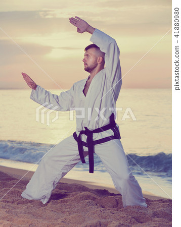 Guy doing karate poses at sunset sea shore 41880980
