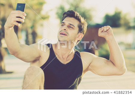 Cheerful man showing biceps taking selfie Cheerful man showing biceps taking selfie 41882354