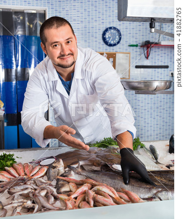 Man in glove behind counter shows fish in his hand 41882765