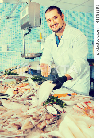 Man in glove behind counter shows fish in his hand Man in glove behind counter shows fish in his hand 41882899